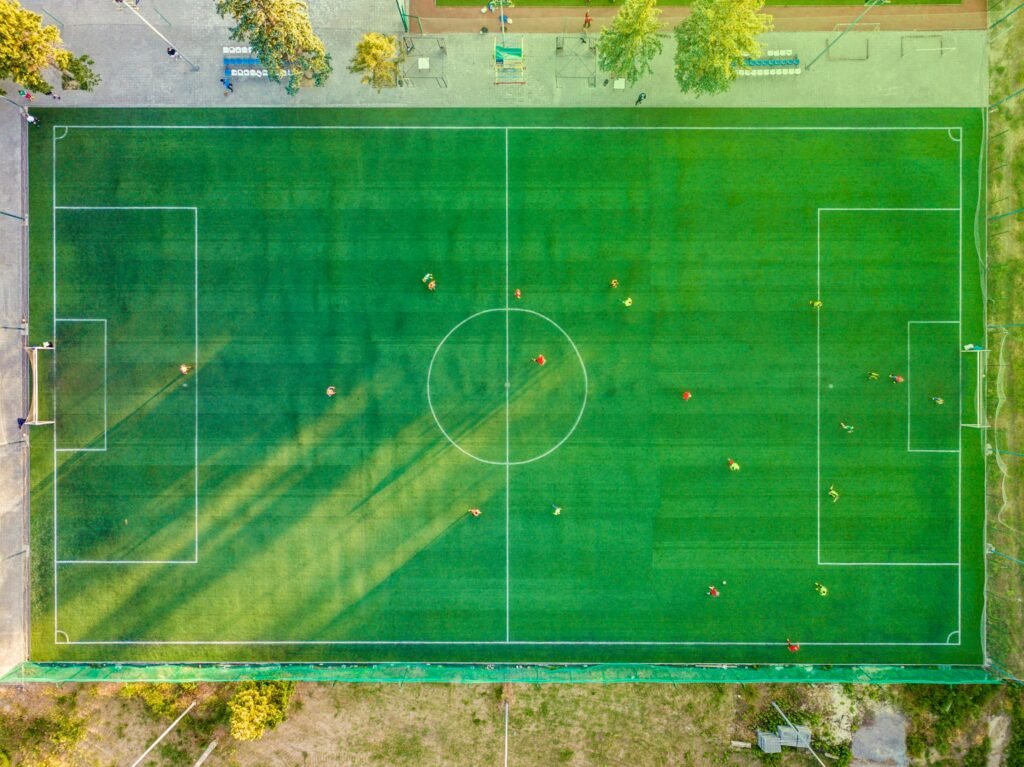 Vista aérea de campo com jogadores em partida, lembrando a origem do futebol